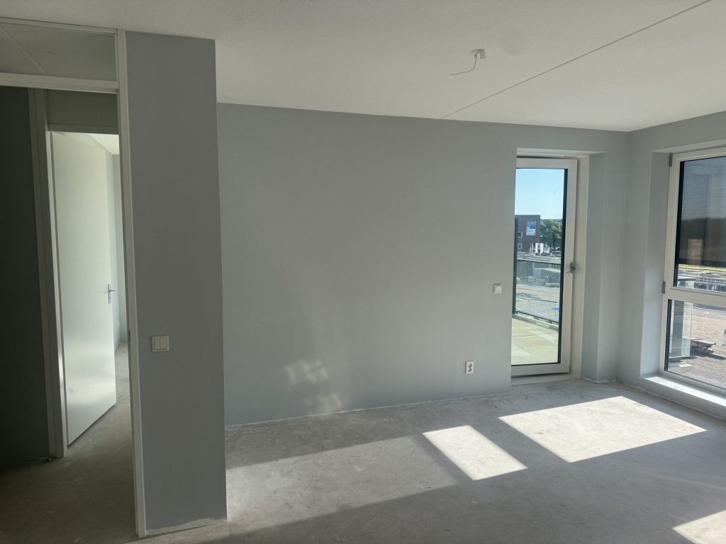Lege nieuwbouwwoonkamer met betonvloer, lichtgrijze wanden en een balkondeur