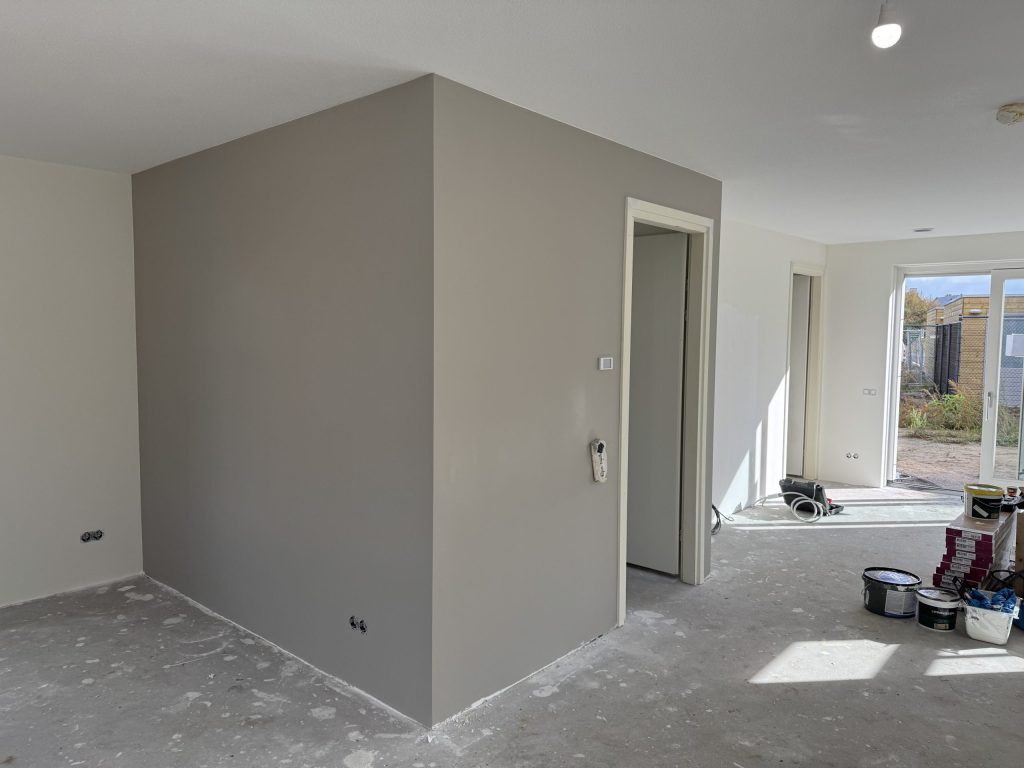 Nieuwbouwwoonkamer met een grijs gesausde wand en een witte wand, met verfemmers op de betonvloer