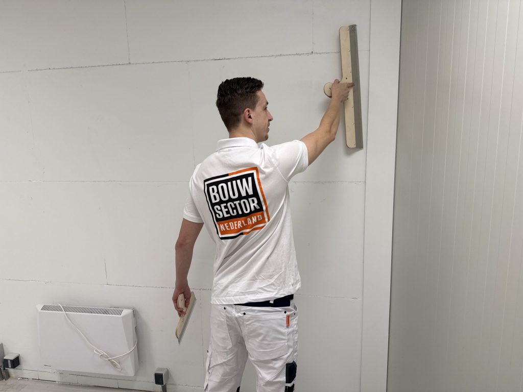 Stukadoor van Bouwsector Nederland strijkt een wand glad met een spaan