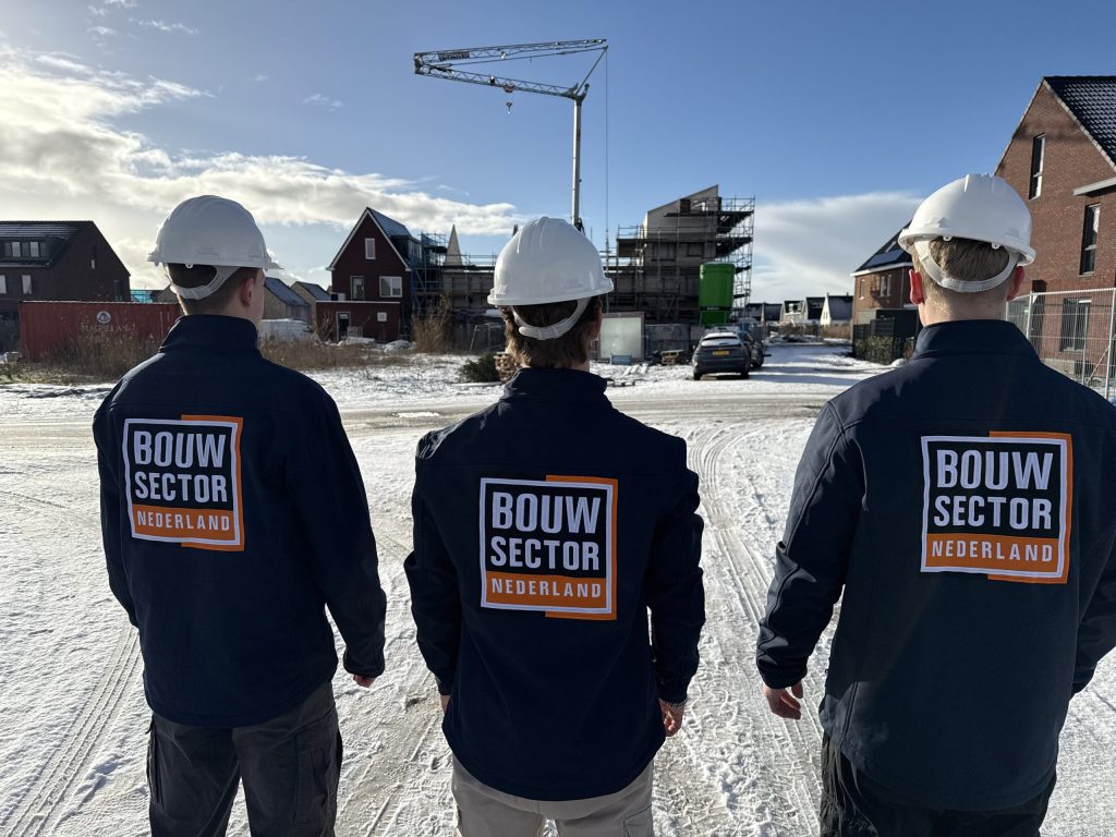 Drie vakmensen van Bouwsector Nederland met witte helm voor een nieuwbouwplaats in de sneeuw
